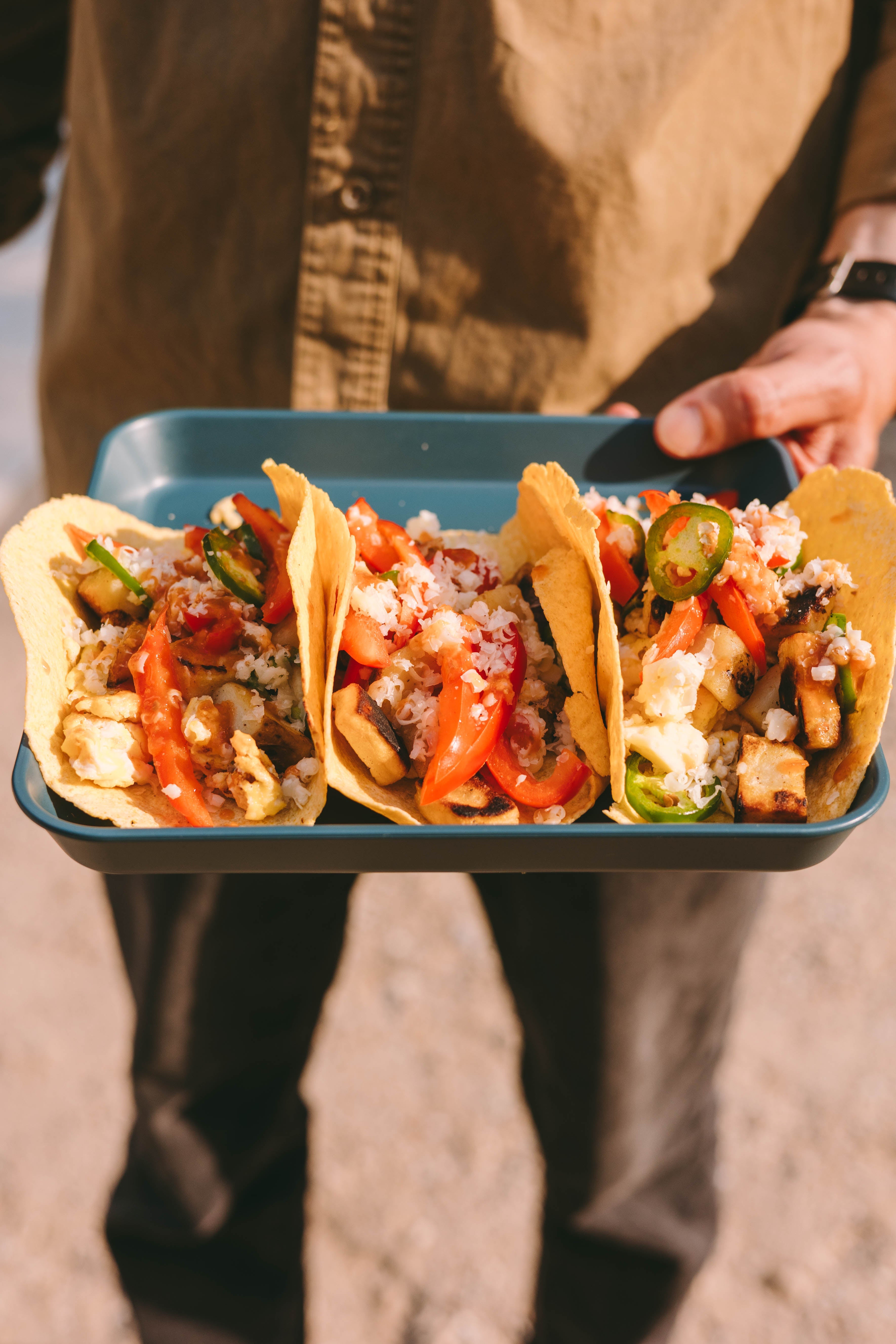A person holding a plate of 3 pieces of breakfast tacos